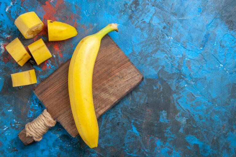 Overhead view of natural grown fresh banan on wooden cutting board on blue background