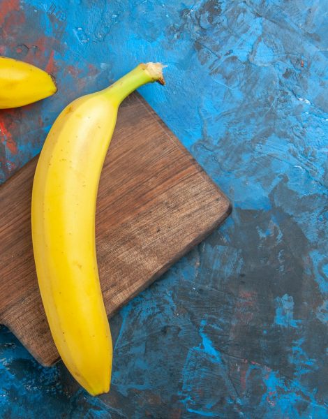 Overhead view of natural grown fresh banan on wooden cutting board on blue background